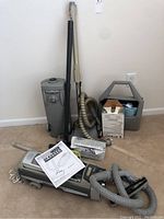 Full lot setup showing Electrolux vacuum, storage container, vacuum bags, wand and hose on carpeted floor.