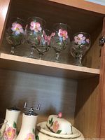 Six painted floral stemware goblets on upper shelf