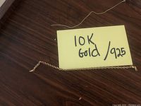 Photo of a broken 10K gold twisted rope chain bracelet next to a note indicating '10K Gold / 925'. The bracelet is incomplete and shows damage near the clasp area.