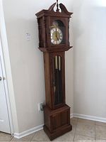 Full front view of tall wooden grandfather clock in corner of room
