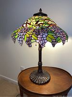 Full view of table lamp showing metal base, slender column, stained glass shade and finial.