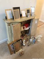Photo showing multiple Lenox picture frames displayed on a small cabinet, with vases, figurines, and decorative items on and inside the cabinet, as well as frames leaning in front.