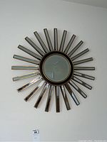 Full front view of sunburst wall mirror showing circular center and radiating mirrored rectangular pieces with gold trim.