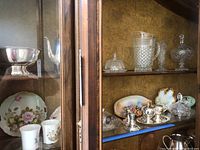 Various crystal, silver plated, and porcelain items in display cabinet including bowls, teapot, plates, and candle holders.