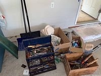 Photo of snow shovels next to kneeling pad and boxes of hand tools, showing general condition and contents of lot