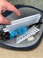 Top-down view inside a zippered pouch showing blue coil rings and perforated metal sheets used in jewelry-making.
