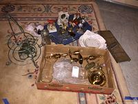 Wide view of lot contents displaying assorted vintage collectibles including glass bottles, brass items in a cardboard box, and napkin holders on a blue tray.