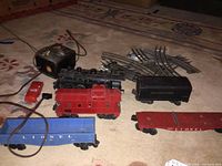 Photo showing most of the train set items including the black engine, red caboose, blue open freight car, red flatcar, black coal tender, red accessory car, transformer, and tracks.