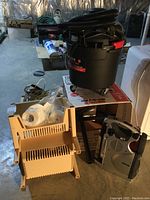 Hoover 6-gallon wet dry vacuum atop box, plastic storage rack, paper towels, and Jeep portable radio with TV and light on basement floor.