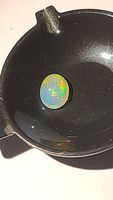 Oval cabochon natural Ethiopian opal showing deep body color and multicolor flash under bright light on a black dish.
