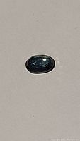 Close-up photo of the deep blue green oval sapphire laid flat showing color and cut.
