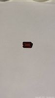 Photo showing the garnet gemstone on a white background, highlighting the rectangular emerald cut and deep cherry red color.