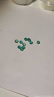 Ten small loose round emerald gemstones on a white background.