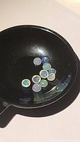 Eleven small round cabochon cut Ethiopian opals shown in a black dish, displaying various plays of color including blue, green, and red hues.