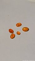Five polished oval-shaped natural Fanta orange fire opal gemstones on a white background, showing color and flash.