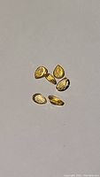 Six pear-shaped golden citrine gemstones on a neutral background, showing their faceted surfaces and size.