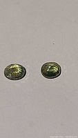 Pair of oval cut green sapphires on white background showing facets and color under light.
