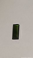 Close-up photo of a single baguette cut forest green tourmaline gemstone on a plain background