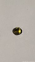 Oval cut sapphire with visible multicoloured hues, greenish-yellow dominant, good clarity and polish, placed on white background.