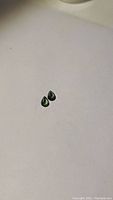 Distant photo of two small pear cut green sapphires on white background, showing their matched shape and color.