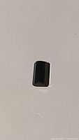 Top view of rectangular emerald cut green tourmaline gemstone on white background, showing the emerald cut facet pattern and deep green color.