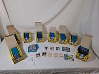 Wide shot of seven open boxes filled with sealed blue Topps baseball sticker packs and several individual baseball player stickers laid out in front.