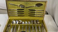 Full view of open silverware case displaying all included cutlery and serving pieces arranged with some knives on top lid and spoons, forks below.