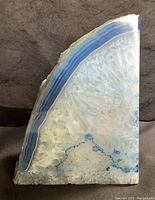 Front view showing polished blue dyed agate with distinctive banding, crystalline interior, and natural rough edge.