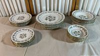 Full set of fine china plates and bowls arranged in groups by size, showing total quantity and condition.