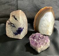 Front view of two polished agate geode bookends, one brown and grey banded and the other dyed purple, with amethyst crystal cluster in front