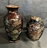 Two vintage Japanese porcelain vases on dark fabric backdrop. Left is taller brown vase with chrysanthemum and quail design, right is smaller lidded black vase with chrysanthemum and dragonfly design.