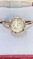 Close-up photo of ring face showing yellow gold band and a large, round faceted faux diamond set in six prongs.