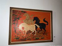 Full view of framed canvas artwork depicting three running horses with grass and foliage details, orange background, wooden frame.