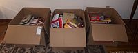 Three cardboard boxes filled with various books and boxed games/puzzles, tightly packed.