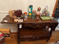 Front view of the wooden buffet showing the decorative carved drawer, bottom shelf with drawer, and items on top.