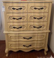 Front view of vintage wood chest of drawers showing the elaborately carved embellished insets on all five drawers and black ornate handles.