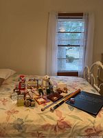 Overview photo of assortment of toys, dolls, and collectibles arranged on floral bedspread, including polar bear plush, Barbie dolls, toy truck and baseball glove bank among others
