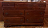 Front view of the wooden dresser showing seven drawers and bracket feet.