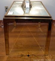 Front view of square mirrored glass top end table with metal legs and frame, sitting on wooden floor underneath a lamp.