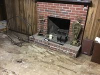 Photo showing the full fireplace setup with the andirons, brass screen, poker, shovel, log holder, and brick hearth.