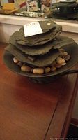 Front angled view of electric indoor fountain showing stacked imitation slate layers and smooth small stones on a black basin placed on wooden surface.