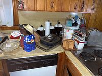 Countertop with glass bakeware dishes, ceramic cookie jar shaped like a boy, metal grater, black and white ceramic canisters, and wooden handled utensils.