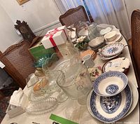 Wide view showing glass serving plates, punch bowl, coffee cups, cake plates, apron set, table linen, and other tableware on dining table.