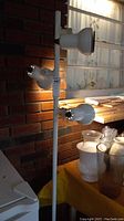 Front view of the white metal floor lamp with three light heads showing the bulb fittings and pole mounted on a round wooden base.
