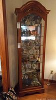 Front view of tall lighted curio cabinet showing glass shelves filled with figurines and collectibles.