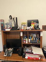 Photo of office desk with computer monitor, wired speakers, desk phone, and various office supplies on shelves including clocks, stationery and organizer items.