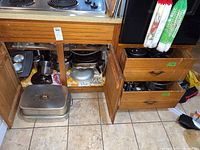Wide angle photo showing wood kitchen cabinet and two drawers filled with various cookware including roaster, pots, pans, and more.