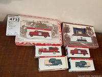 Photo showing all six boxed model vehicles including fire trucks and classic cars arranged on a surface.