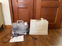 Singer Simple 3221 with foot pedal, cloth cover, and manuals displayed on hardwood floor against closed wooden doors.