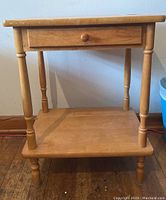 Front view of square wooden table showing drawer and bottom shelf with turned legs.